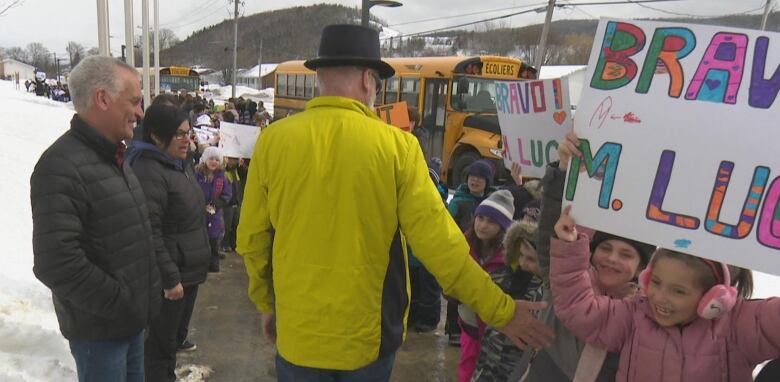 Dozens of students line up with handmade signs as a man in a top hat walks by. 