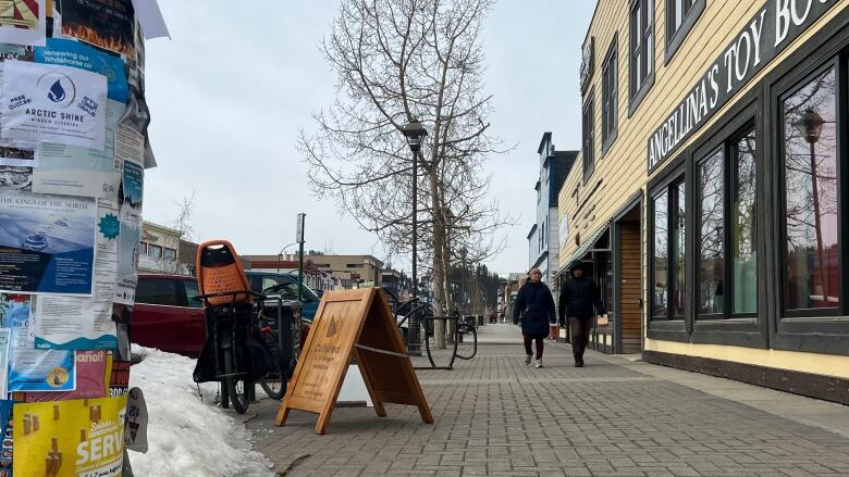 Two pedestrians are seen walking along a downtown sidewalk lined with businesses.