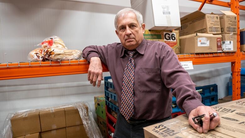 An older man standing with a lack of food and boxes in a warehouse. 