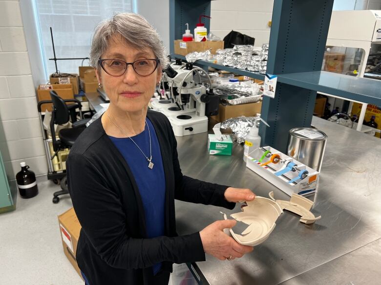 A woman stands holding a cut-up brown paper bowl with lab benches and equipment in the background.