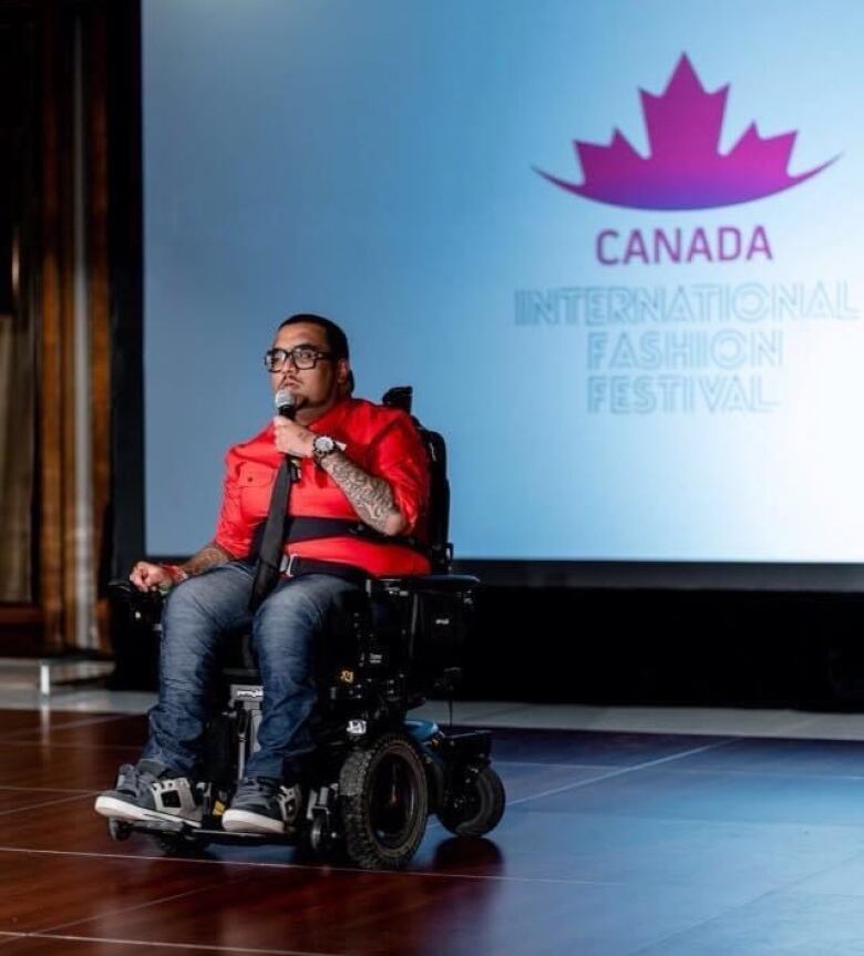 A man in a wheelchair holds a microphone on stage.