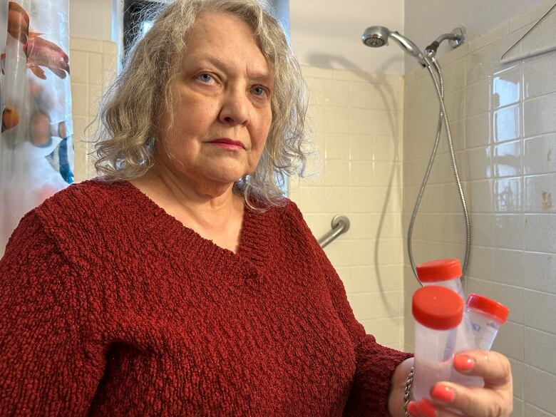 A woman stands by a show holding up three tubes of water. 