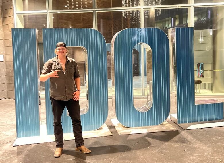 A young man stands in front of a big sign that says IDOL