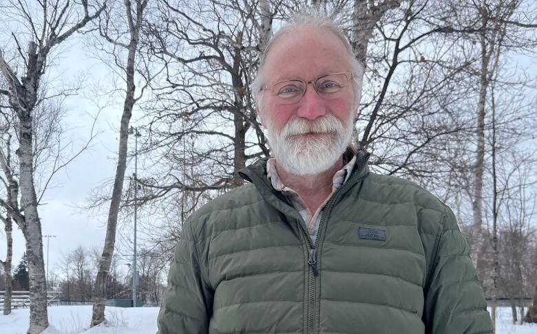 A man with glasses stands outdoors looking at the camera