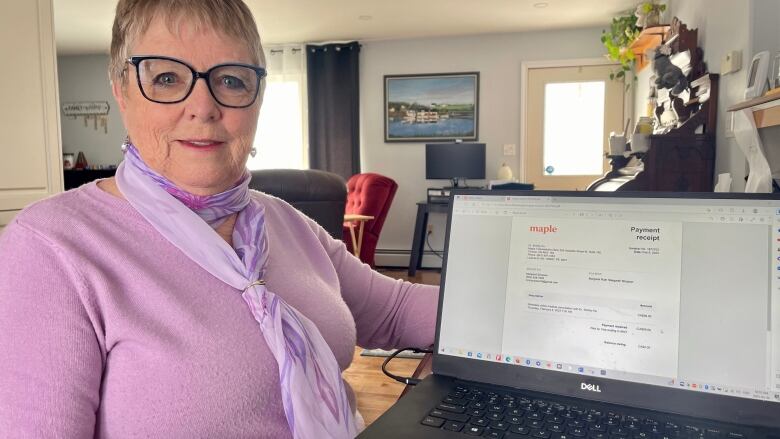 A woman posing for a picture while holding a laptop showing a document with the Maple logo in its header.