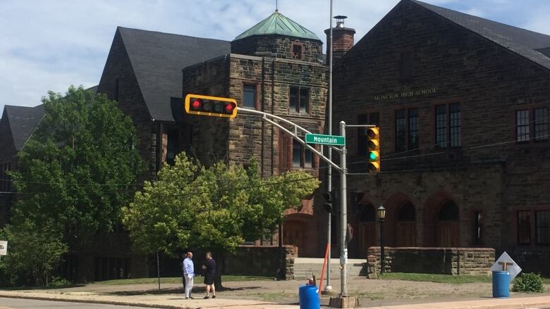 A three-storey brick building on a street corner with a traffic light in the foreground and two people standing on the sidewalk. 