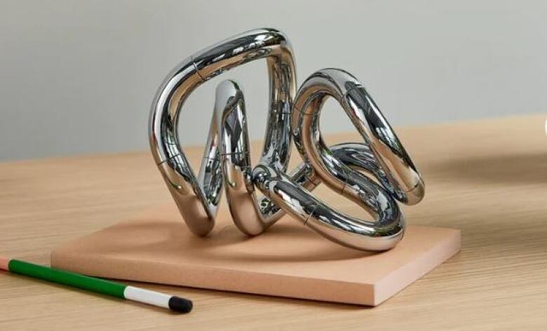 A piece of twisted, metal chrome is pictured on a light wooden desk.