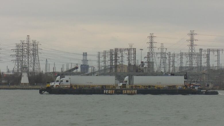 A boat carrying two transport trucks on the Detroit River.