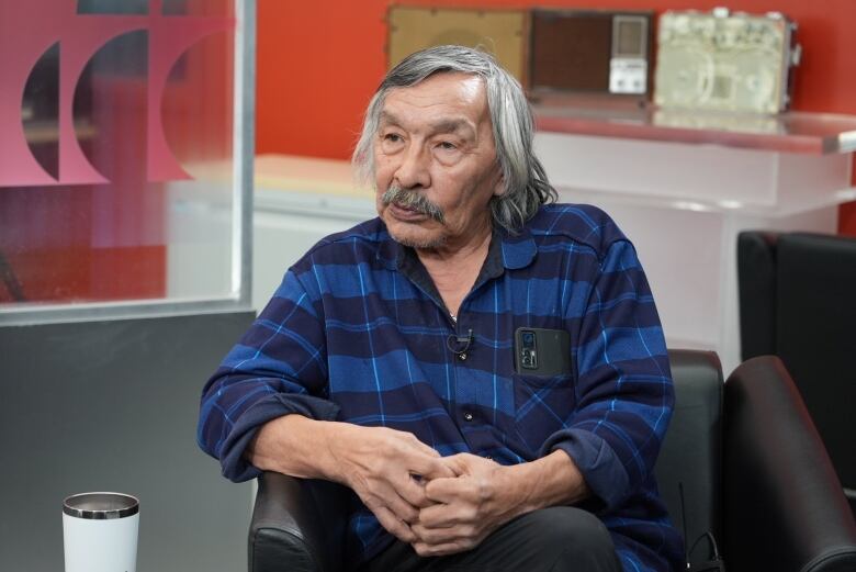 Man with grey and white hair sits in chair.