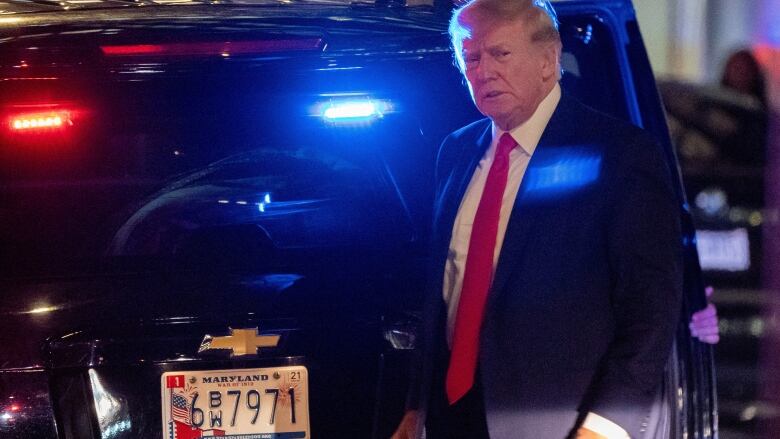 Donald Trump stands next to SUV with lights flashing blue and red. 