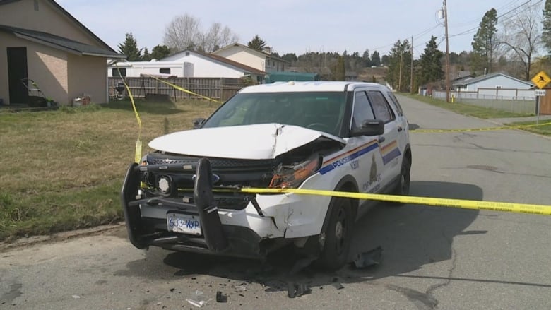 A police SUV has its front smashed while parked on a side street. Police tape is draped over it.