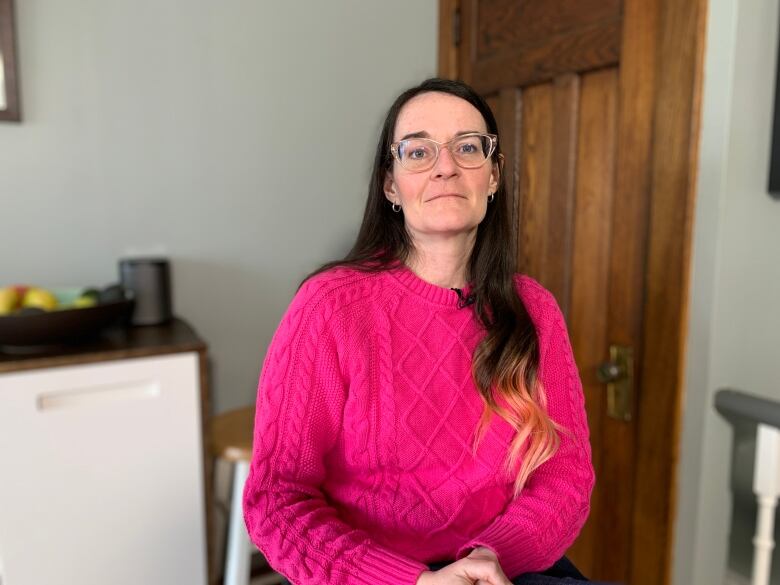 Teresa Miller sits in her kitchen in a pink sweater, looking up.