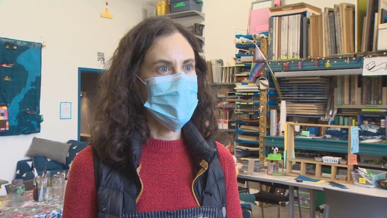 A woman with a medical mask on stands in an art studio.