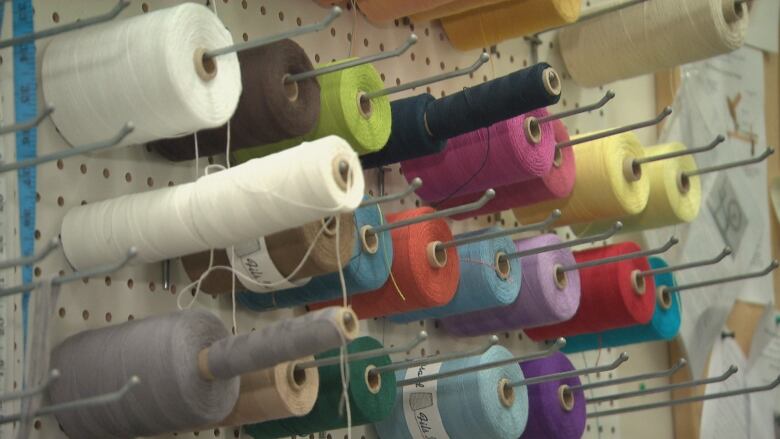 Colourful spools of thread sit on a wall rack.