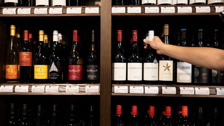 A hand grips a bottle of wine among many bottles on the shelves.