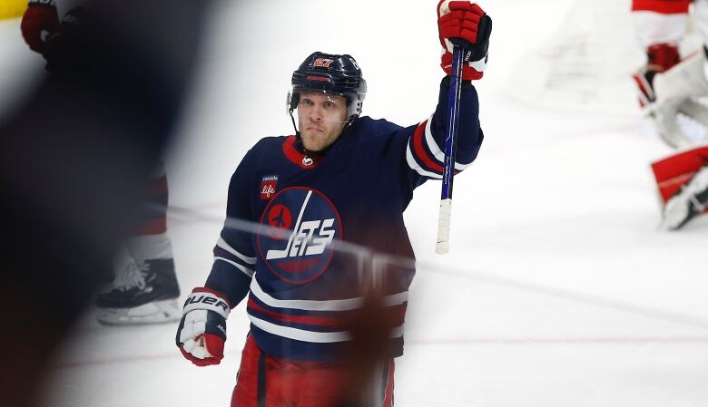 Nikoljah Ehlers wears the Winnipeg Jets reverse retro jersey, which is navy blue, and celebrates a goal with an arm in the frame. 