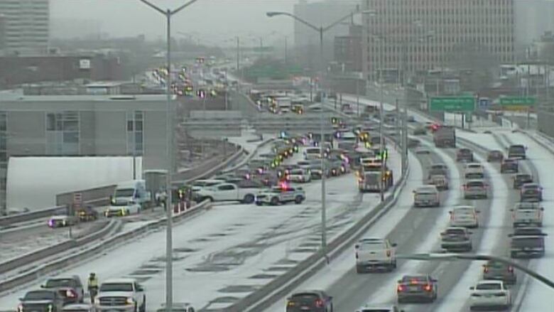 A traffic camera shot of a collision closing part of a snowy highway in a city.