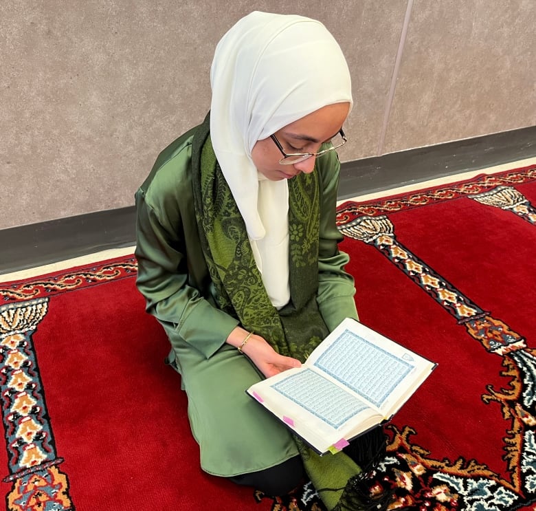 Woman, holding a book, sits on a carpet