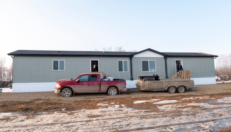 A red truck that has a trailer attached to it is parked in front of a one-storey home, with two doors, on James Smith Cree Nation. 