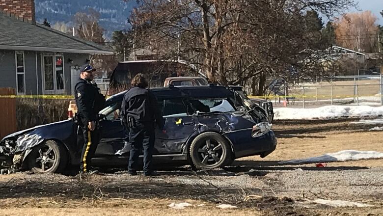 Two police stand beside a smashed vehicle.