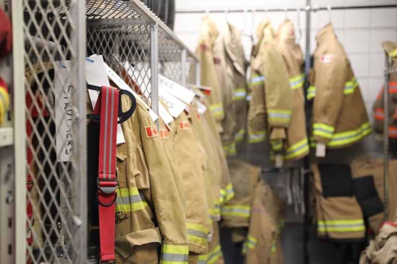 Firefighting jackets, each labelled with a name, hang in a row in a storage room.