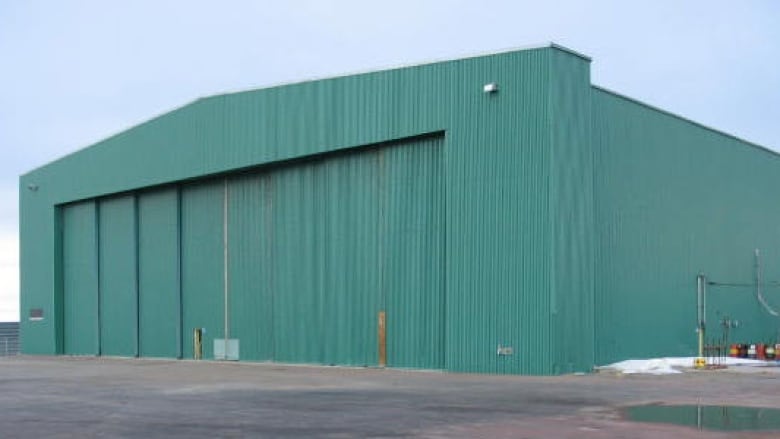 A large green airplane hangar is seen from the outside.