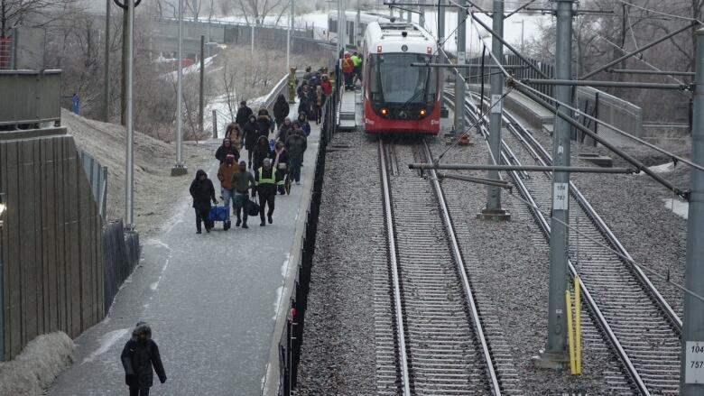 People walk beside train tracks and a stopped light rail train.