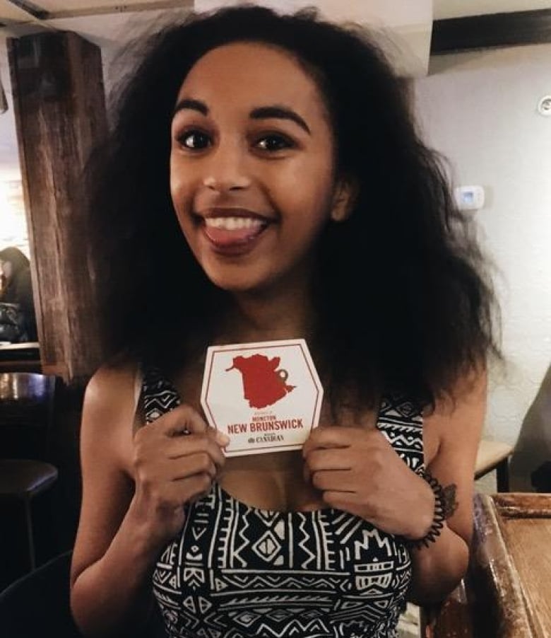 A woman stands in a bar holding a coaster that says 