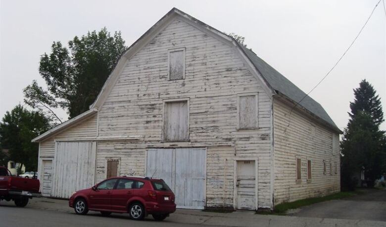 A red SUV sits before a 114-year-old white barn with peeling paint. 