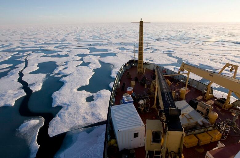 A photo taken from onboard a ship, looking down at its bow as it cuts through icy water.