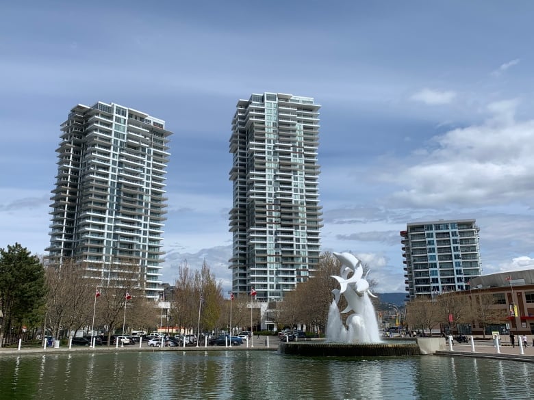 Three condo buildings with a pond and a dolphin-shaped statue in front of it.