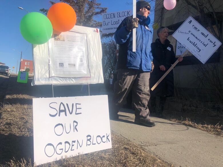 A sign that reads 'save our Ogden Block,' is put into the grass. It has green and orange balloons on top. 