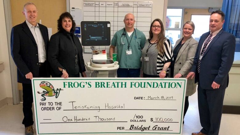 Six people standing around a giant cheque in a hospital.