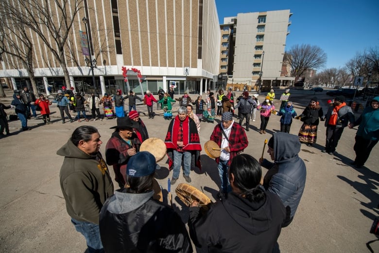 Drummers stand in a circle on a street, with other protesters in a circle around them.