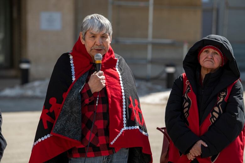 A person wrapped in a red and black blanket speaks into a microphone.