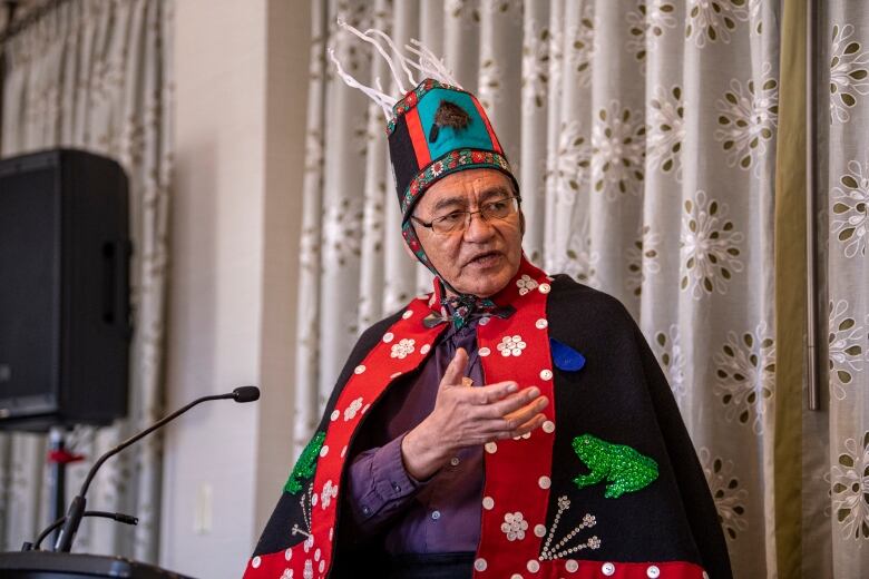 A Wet'suwet'en chief in traditional regalia speaks at a microphone.