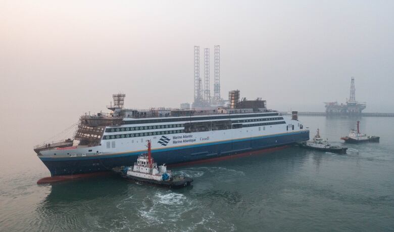 A 203-foot ferry with Marine Atlantic lines and logo in waters off China, accompanied by three smaller boats as it is floated from dry dock.