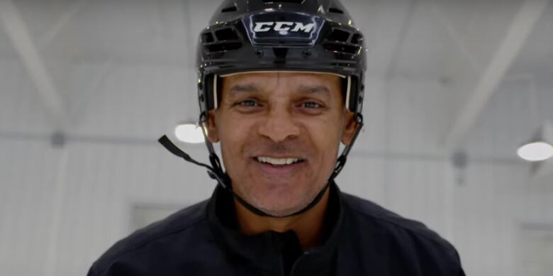 A man wearing a black jacket and helmet smiles at the camera.