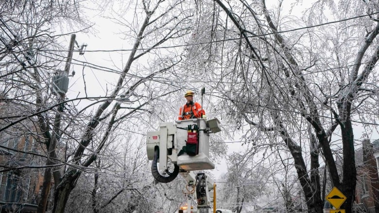 hydro worker in cherrypicker truck in middle of street with icy trees