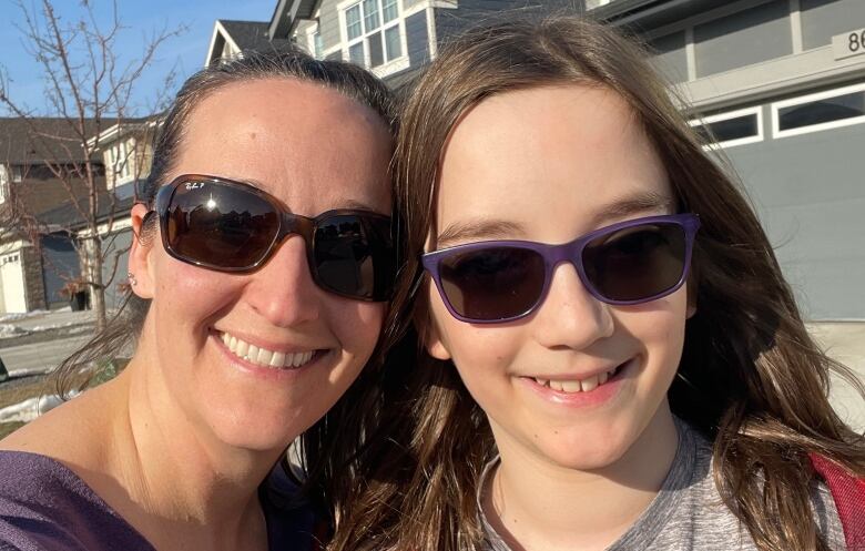 Candice and her son Keegan look straight into the camera, wearing sun glasses and standing in front of a row of houses.