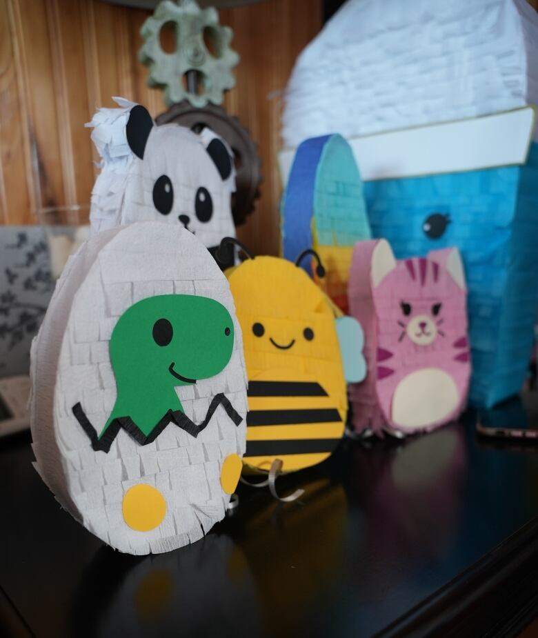 Colourful pinatas shaped like bees, kittens and dinosaur eggs line up on a table.