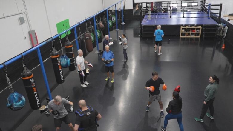 A group of people stand around a boxing gym sparring.