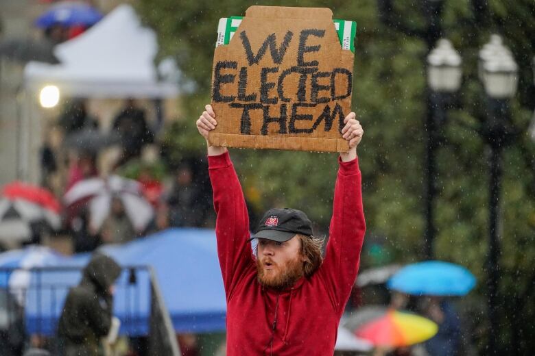 Bearded man in red shirt holding sign that reads We Elected Them 