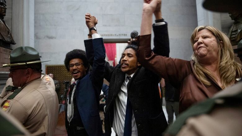 Two Black men and a white woman stand with hands joined and raised in victory