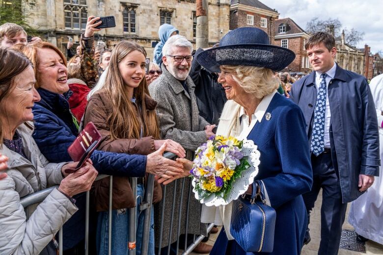 A person holding a bouquet of flowers meets people lined up to meet them.