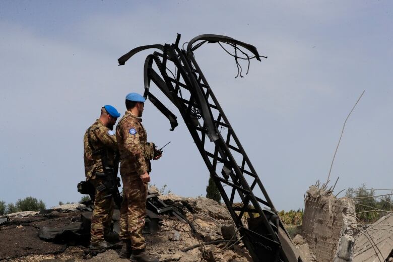 Peacekeepers in blue berets and military fatigues inspect damage. 