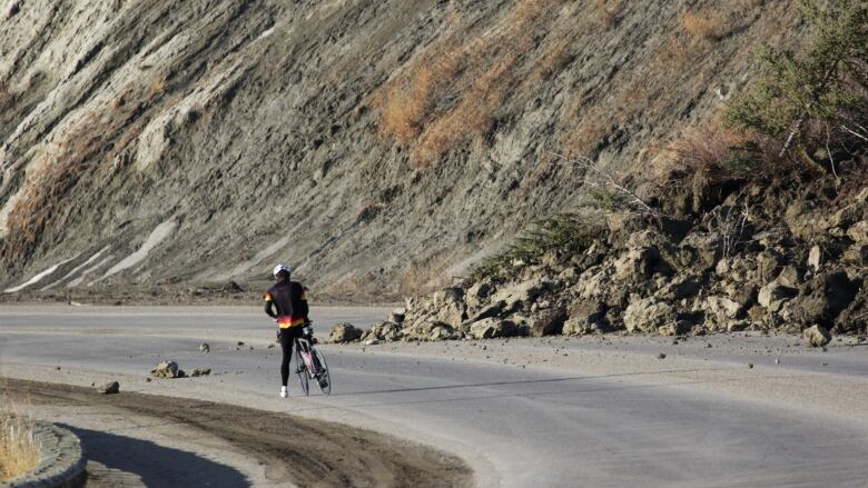 The photo shows a cyclist stopped next to debris from a landslide. 