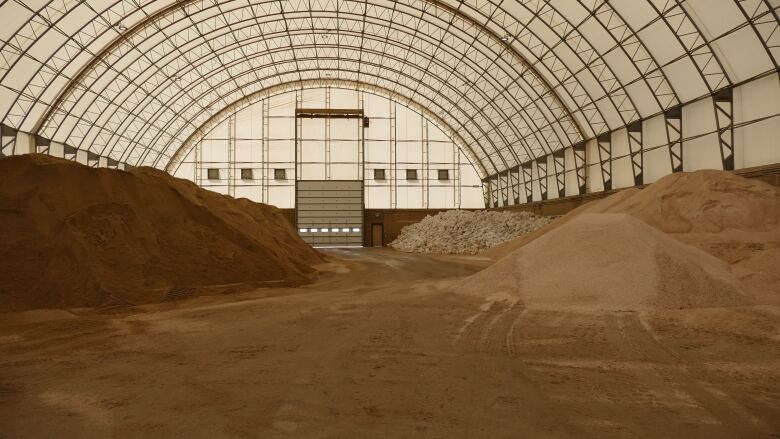 Large piles of sand, dirt and sandbags inside a large building with a curved roof.