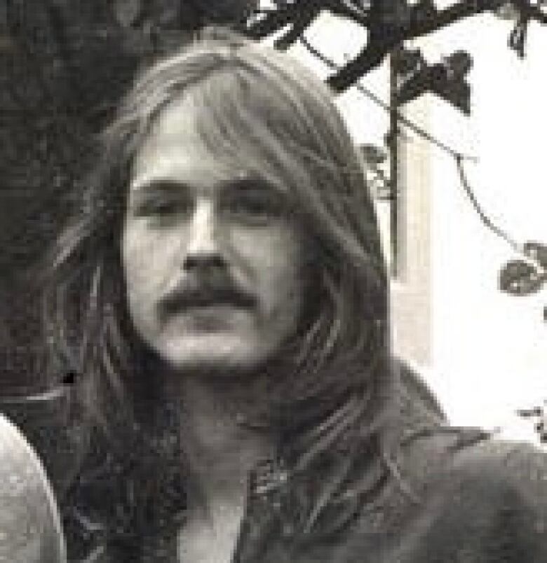 A black-and-white photo of a man with long hair and a mustache.