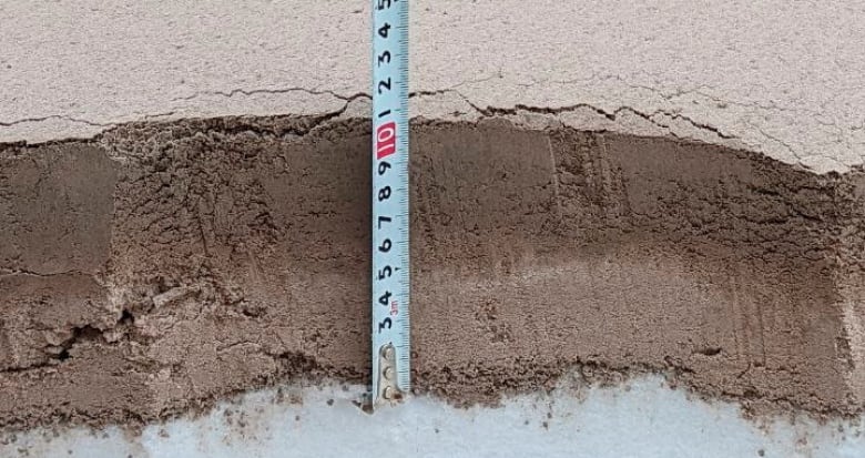 A white measuring tape held against a thick layer of brown ash on the ground.